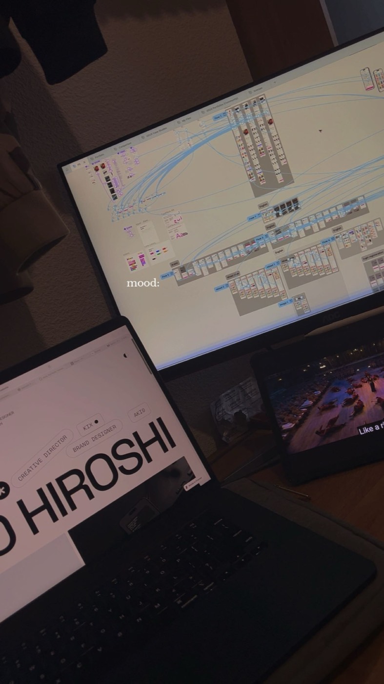 A desk at night — two monitors and a laptop, design files open across all three